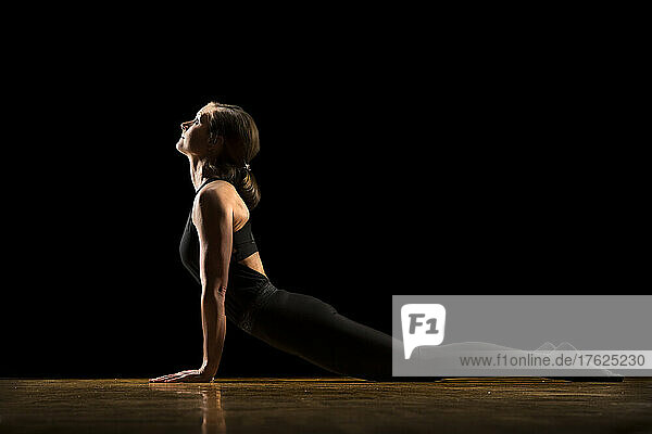 Woman practicing cobra pose against black background