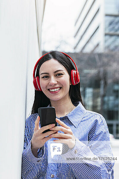 Smiling woman holding mobile phone listening music through wireless headphones