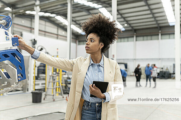 Businesswoman holding tablet PC analyzing machine in factory