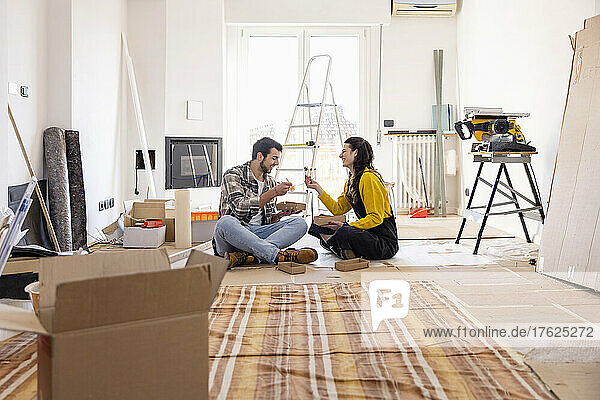 Young couple eating food sitting on ground at new home