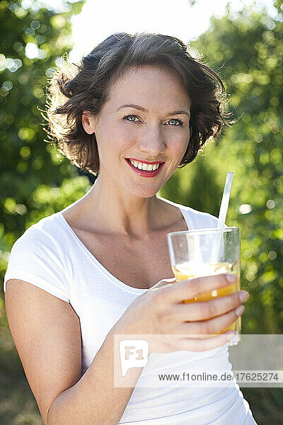 Happy woman with orange juice standing by trees