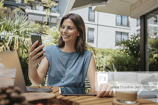 Lächelnde Geschäftsfrau bei Videoanruf über Smartphone im Hinterhof