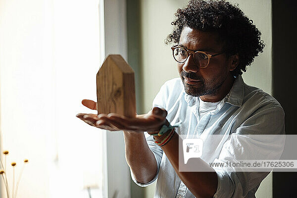 Man with hands cupped looking at model house at home
