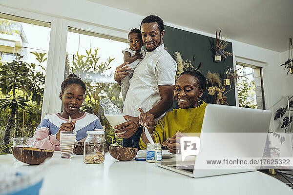 Father with milk bottle by mother and daughter having breakfast at home
