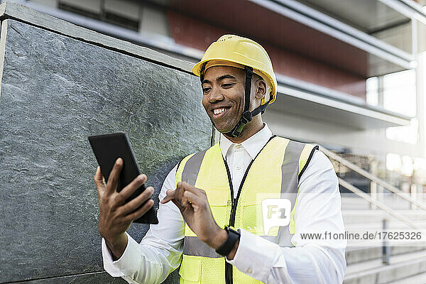 Smiling engineer using tablet PC standing by wall