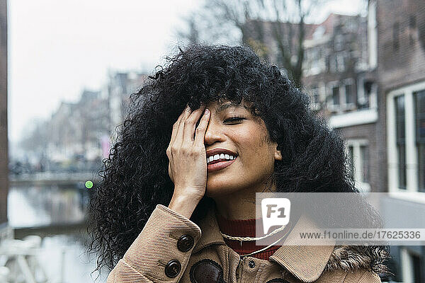Beautiful woman with curly hair covering eye with hand