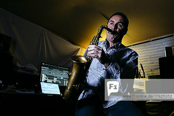 Saxophonist playing saxophone sitting in recording studio