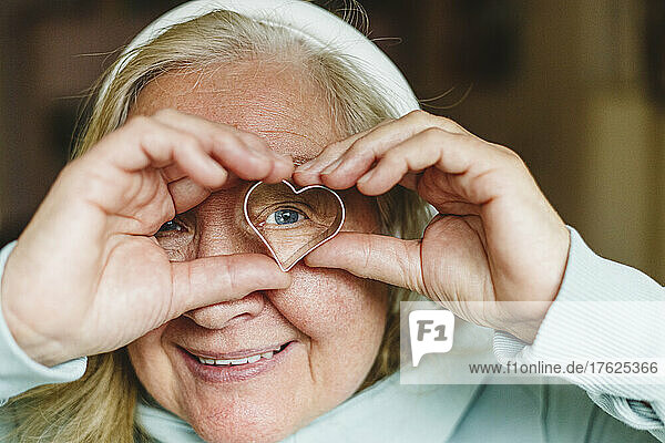 Smiling senior woman looking through heart shaped cookie cutter