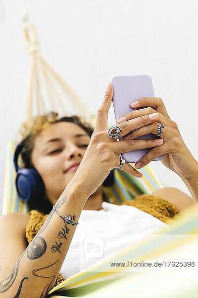 Woman with tattoo on arm using smart phone on hammock