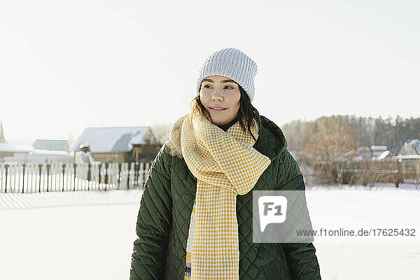 Woman wearing knit hat and scarf standing at snowy garden