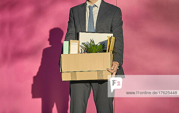 Businessman carrying box with personal belongings on sunny day