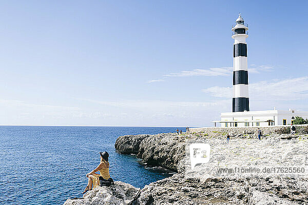 Woman sitting on rock looking at seascape on sunny day  Artrutx Lighthouse  Minorca  Spain