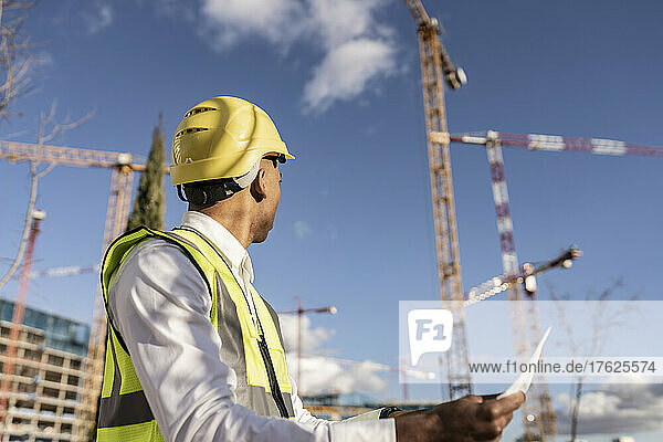 Architect wearing hardhat working at construction site on sunny day