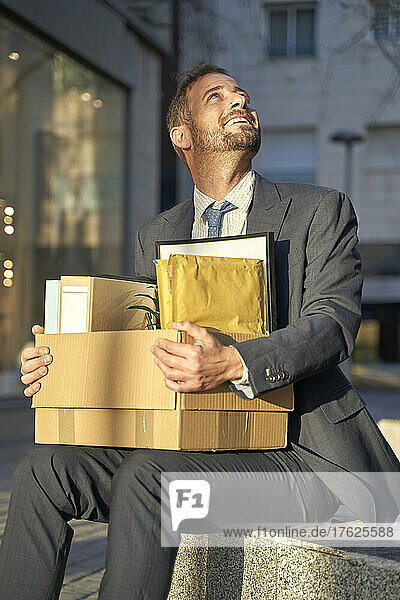 Smiling businessman with box sitting on bench