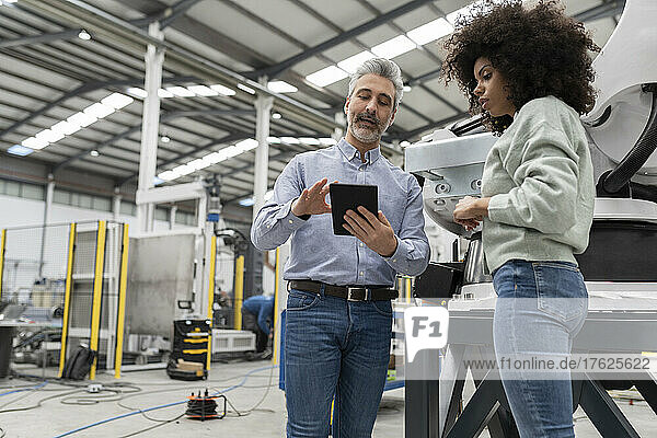 Engineer showing tablet PC to developer standing in factory