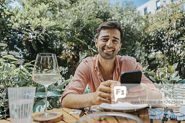 Happy man with mobile phone at outdoor table