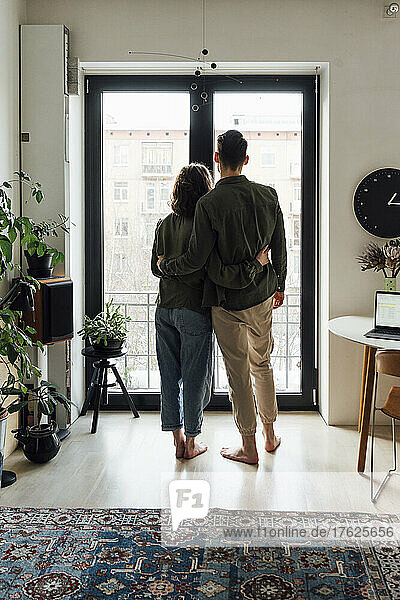 Young couple standing together by glass window at home