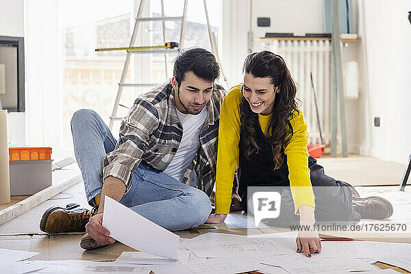 Smiling woman discussing over floor plans with boyfriend at new home