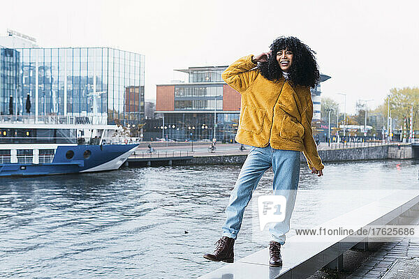 Happy woman walking on bench by canal in city