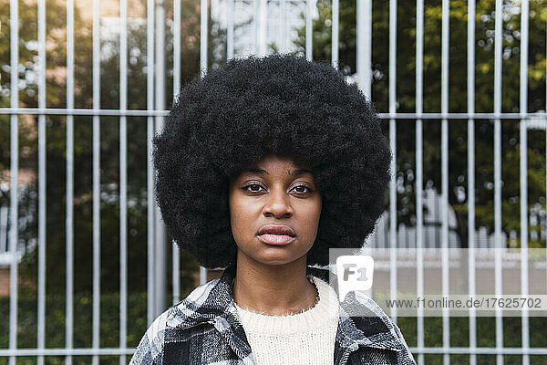 Serious woman with afro hairstyle in front of fence