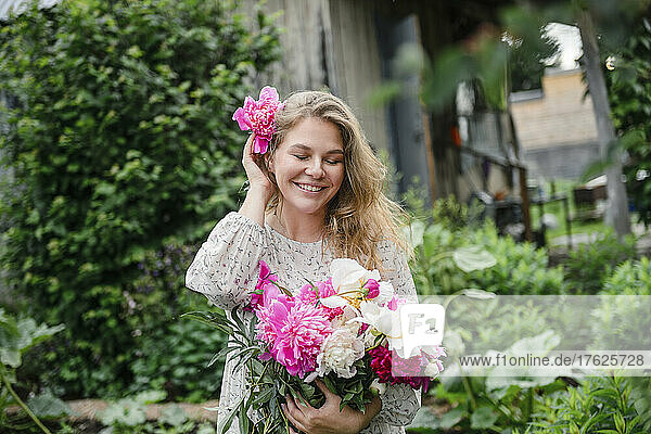 Beautiful smiling blond woman wearing pink flower standing in garden