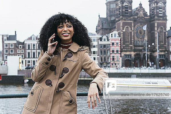 Happy young woman talking on mobile phone by railing in city