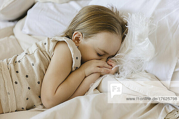 Girl with feather sleeping on bed at home
