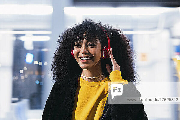 Happy woman with curly hair enjoying music through wireless headphones at night