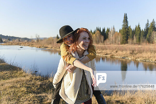 Glückliche Frau trägt ihre Freundin huckepack am Fluss entlang