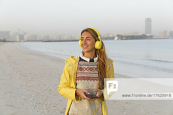 Happy woman with smart phone and yellow headphones at beach