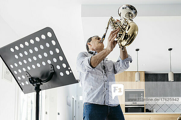 Passionate musician with eyes closed blowing saxophone at home