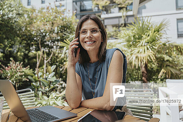 Lächelnde Geschäftsfrau  die im Hinterhof mit dem Smartphone spricht