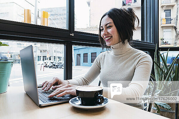 Happy businesswoman using laptop sitting in cafe