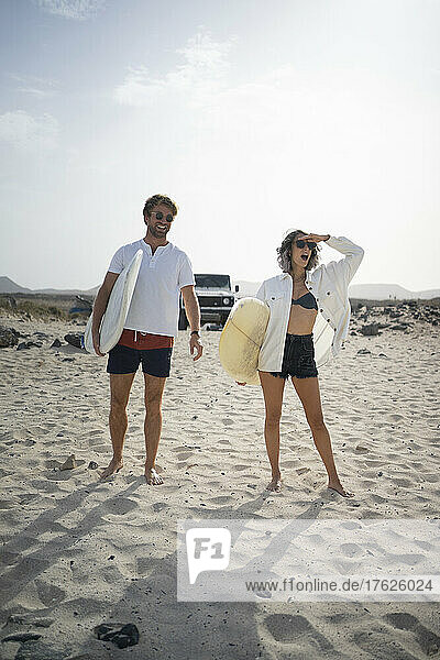 Happy couple standing with surfboard at beach on a sunny day