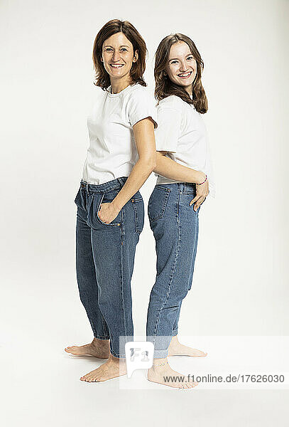 Happy girl with mother standing with hands in pockets by white background