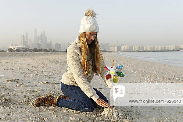 Happy woman sitting on sand with multi colored pinwheel toy at beach