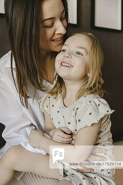 Smiling woman sitting with cute daughter at home