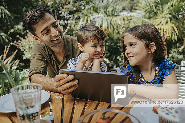 Glücklicher Vater und Kinder mit Tablet-PC im Garten