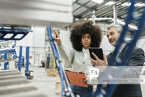 Technician showing machine to businessman with tablet PC in factory