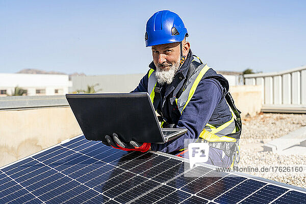 Smiling technician with laptop working at solar power station