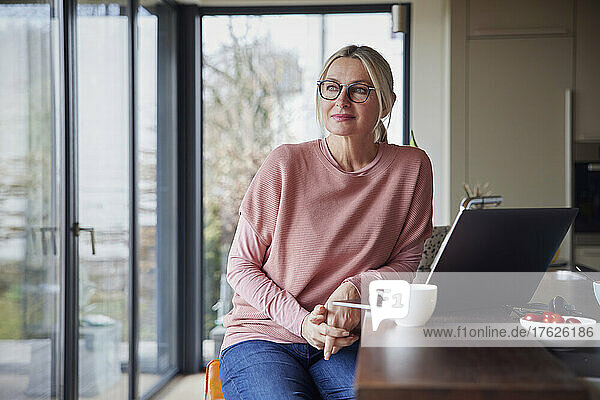Blond woman wearing eyeglasses sitting with laptop kitchen