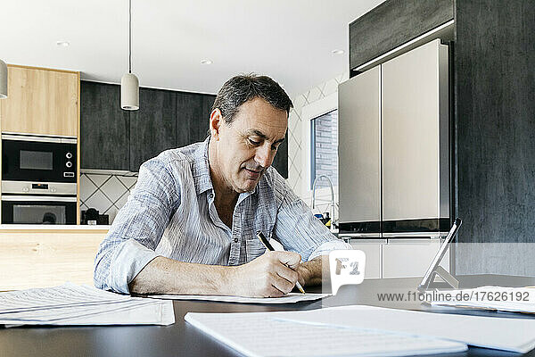 Mann schreibt Musiknoten und sitzt mit Tablet-PC in der Küche am Tisch