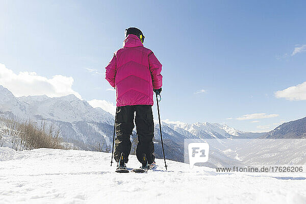 Man holding ski poles looking at mountain standing on snow in winter