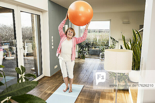 Happy senior woman exercising with fitness ball at home