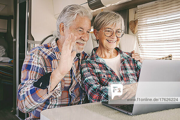 Smiling senior man and woman on video call on laptop in camper van