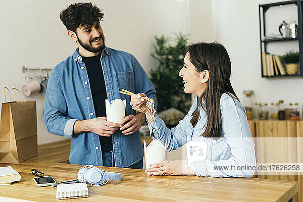 Smiling couple having noodles in kitchen at home