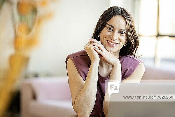 Smiling businesswoman with hand on chin sitting at home