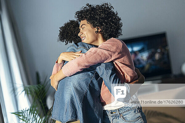 Happy woman embracing girlfriend standing in living room at home