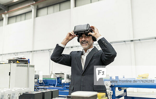 Happy businessman removing virtual reality simulator standing in factory