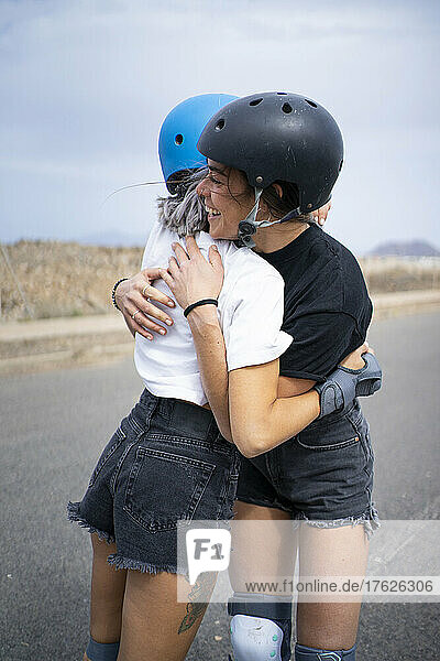 Friends wearing helmets hugging each other on road